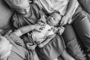 Three children hold their newborn sibling in their laps