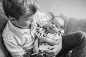 A boy cradles his newborn baby sister in his lap sitting on a beanbag