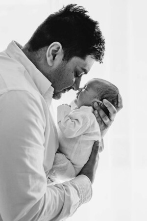 A father gently presses his nose to his newborn baby's face and holds her close