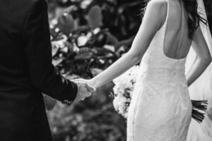 Black and white detail photo of a bride and groom holding hands as they walk