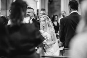 A bride walks down the aisle towards her groom surrounded by wedding guests in a church
