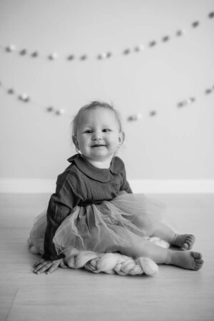 Black and white photo of a baby girl wearing a tulle dress and sitting on a blanket for a sitter session