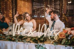 A couple share a celebratory fist bump at their wedding reception with a neon Mr and Mrs sign