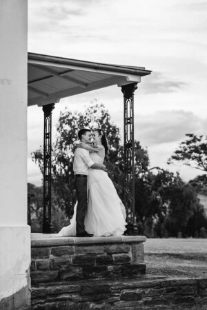 A bride and groom stand on the Gledswood Estate veranda at sunset after their wedding