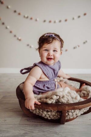 A little girl sits on a white knit blanket in a round bowl for her first birthday studio session