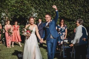 A couple walk back down the aisle after their wedding ceremony and the groom pumps his fist in the air in celebration