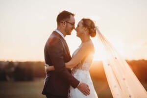A married couple stand with noses pressed together as the sun sets behind them