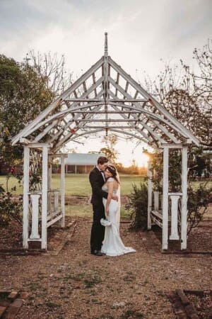 A newly married couple stand cuddling under a white gazebo at sunset on the Gledswood Estate