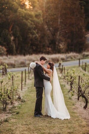 A couple stand in a vineyard at Gledswood and hug after they got married at sunset