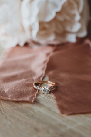 A bride's engagement ring sits on a pink ribbon attached to her bouquet sitting on a table