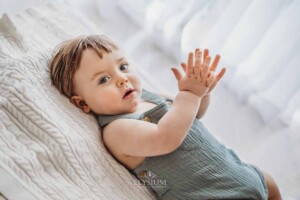 A baby boy in a soft green romper laying on a blanket clapping his hands