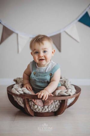 A smiley baby sitting in a big wooden bowl with bunting in the background
