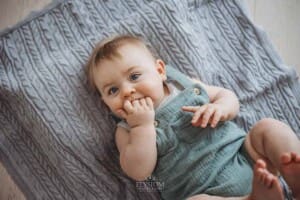 A baby laying on his back on a grey blanket sucks his fingers