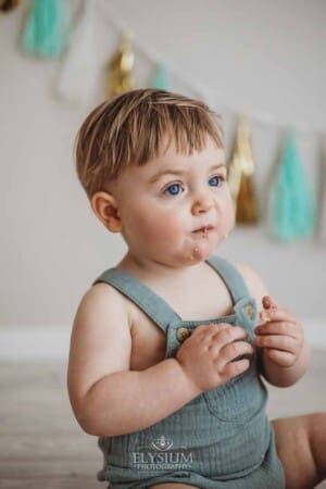 A baby boy smashes into his first birthday cake sitting on a studio floor