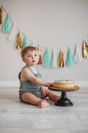 A baby boy sits beside a birthday cake and smashes into it with his hand