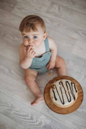 A baby eats birthday cake that he's smashing on a studio floor