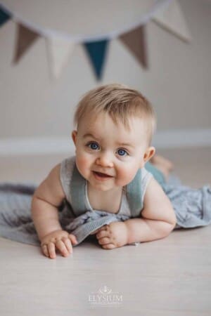 Photo of a happy baby boy laying on his tummy on a grey blanket