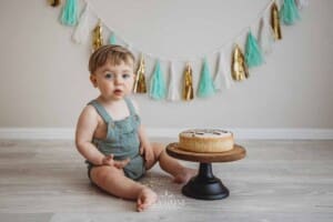 A baby boy sits on a studio floor with a birthday cake that he's about to smash