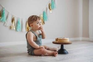 A baby boy sits on a studio floor and smashes his first birthday cake