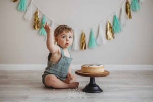 A baby boy sits on a studio floor with a cake that he is about to smash
