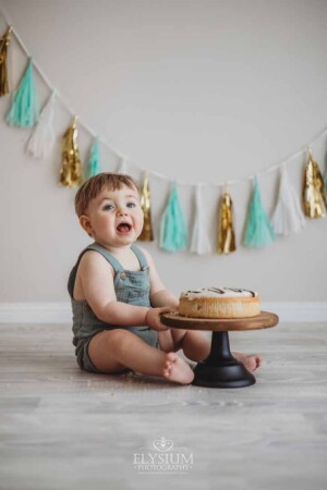 A baby laughs as he smashes into his birthday cake at a milestone session