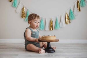 A baby sits facing his first birthday cake and gets ready to smash it