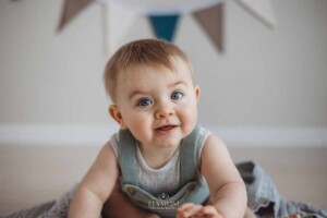Portrait of a smiling baby boy sitting in a studio prop with bunting in the background