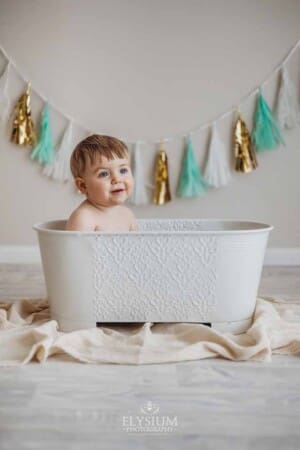 A baby boy washes off in a white bathtub after smashing his birthday cake