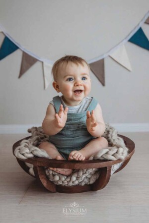A baby sitting in a large wooden bowl claps his hands and smiles