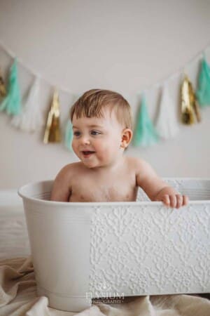 A baby smiles as he sits in a prop bathtub after his cake smash