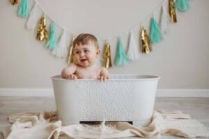 A baby boy plays with water in a prop bathtub and giggles