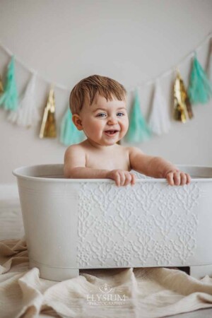 A baby giggles as he sits in a vintage tub washing off after his cake smash
