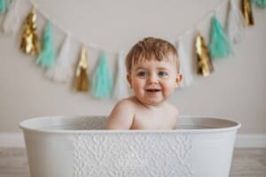 A smiley baby sits in a vintage bath tub prop in a bright studio