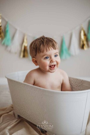 A happy baby boy sits in a prop bathtub after smashing his first birthday cake
