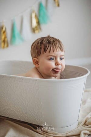 A baby pokes out his tongue and blows raspberries as he sits in a bathtub