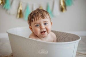 A baby giggles as he sits in a vintage bathtub prop in a bright studio