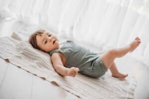 A baby boy lays on his back on a white blanket beside a large window