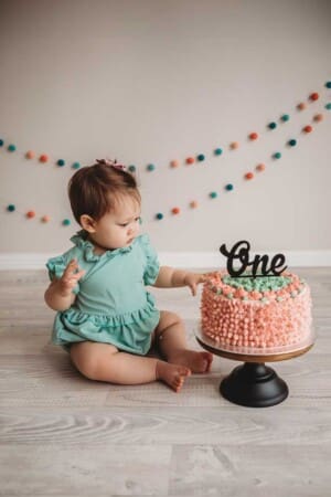 A baby girl inspects her colourful birthday cake before smashing into it