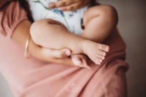 A mother holds her baby girls feet as she sits in her lap for their studio photos