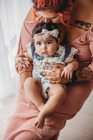 A mother holds her baby girl in her lap as they sit in a studio for photos