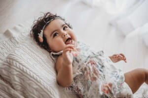 A smiley baby wearing a floral romper lays on a white blanket in a bright studio