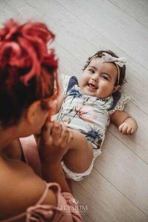 A baby lays on her back giggling while her mother blows raspberries on her feet