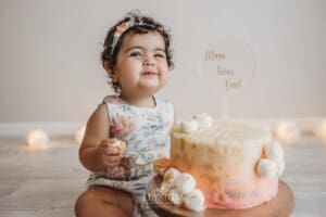 A baby girl grins as she eats her first birthday cake with her hands