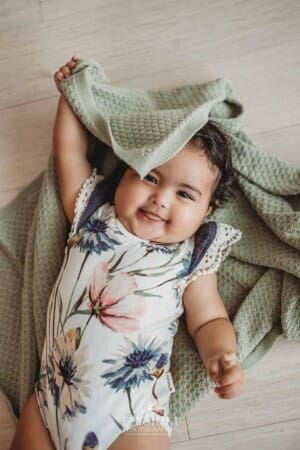 A little girl in a floral romper plays peek-a-boo under a green blanket