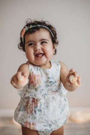 Baby girl giggles as she holds cake during her first birthday cake smash session