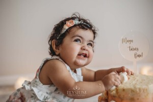 A baby girl grins as she smashes into her first birthday cake