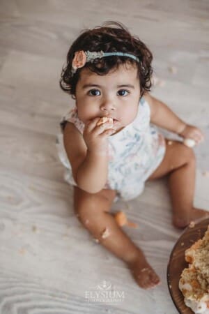 A baby girl puts a handful of cake in her mouth during her first birthday session