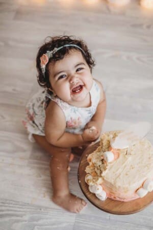 A baby girl gleefully smashes her first birthday cake for her milestone birthday session