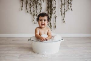 A baby smiles as she sits in a vintage bath tub to clean up after her cake smash