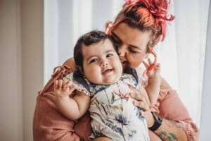 A mother holds her baby girl and kisses her cheek during a studio session